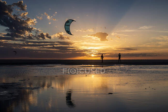 Силуэт двух кайтсерферов на закате, пляж Лос-Лансес, Фауфа, провинция Кадис, Андалусия, Испания — стоковое фото