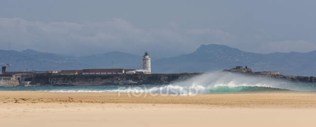 Crashing waves on beach by lighthouse, Tarifa, Cadice, Andalusia, Spagna — Foto stock