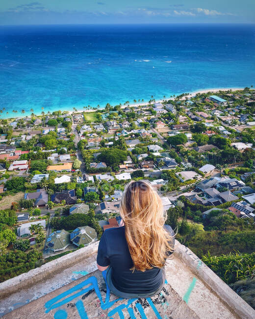 Vista trasera de una mujer sentada en un búnker mirando la vista de la bahía de Kailua, Oahu, Hawái, EE.UU. - foto de stock