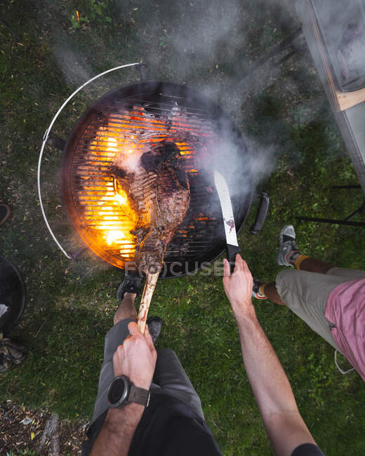 Overhead view of two people cooking meat on a barbecue in the garden, USA — Stock Photo
