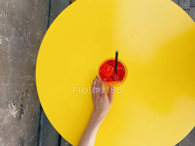 Overhead view of a woman reaching for an aperol spritz cocktail on yellow table — Stock Photo