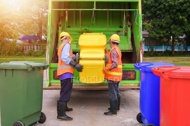 Camión de basura reciclable y el guardián en el village.Garbage colector en el camión de basura. Barredora o trabajador están cargando residuos en el camión de basura portador. - foto de stock