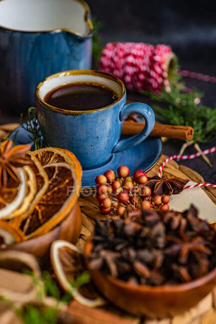 Weihnachtlicher Gewürzkaffee in blauer Keramiktasse zwischen Gewürzen und Beeren auf dunklem launischen Hintergrund — Stockfoto