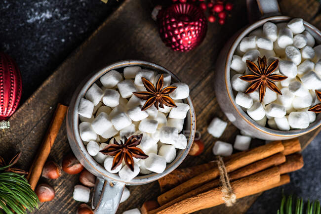 Becher voller Mini-Marshmallows mit Gewürzen auf dunklem Hintergrund als weihnachtliches Essenskonzept — Stockfoto