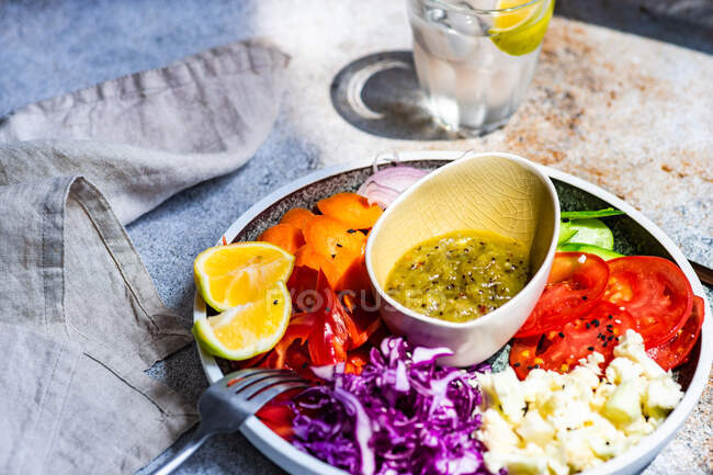 Dîner sain avec bol de légumes bio servi sur une table avec des graines de sésame et un verre d'eau de citron — Photo de stock