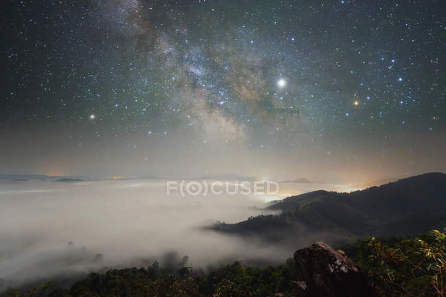 Scena notturna di esposizione lunga di scena montuosa con basse nuvole e stelle della Via Lattea in cielo — Foto stock