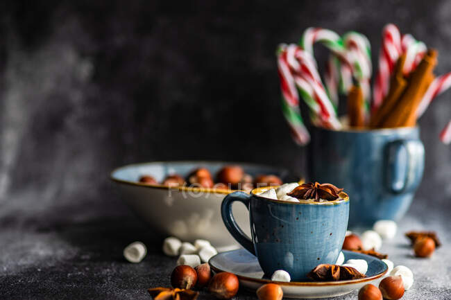 Tazas llenas de mini malvaviscos con especias sobre fondo oscuro como concepto de comida navideña - foto de stock