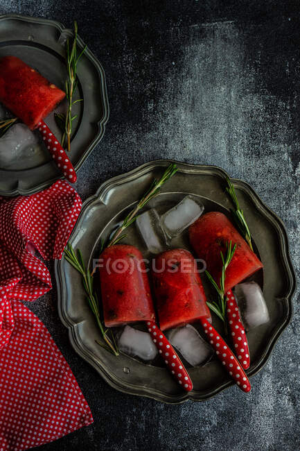 Postre de verano con paletas de sandía orgánicas servidas en plato con hielo y romero - foto de stock