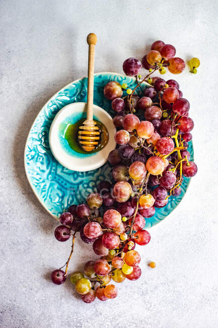 Vista dall'alto di grappolo d'uva rossa su piatto con ciotola di miele — Foto stock
