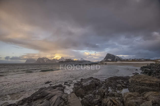 Scène de plage rocheuse avec montagnes au coucher du soleil, Stor Sandnes, Flakstad, Lofoten, Nordland, Norvège — Photo de stock