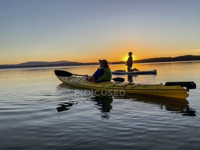 Couple paddleboarding and kayaking in ocean at sunset, Canada — Stock Photo