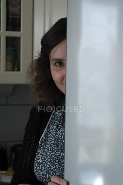 Porträt einer lächelnden Frau, die sich hinter einer Tür in einer Küche versteckt — Stockfoto