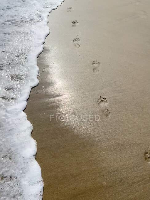 Pegadas na areia molhada com onda de espuma do mar rolante — Fotografia de Stock