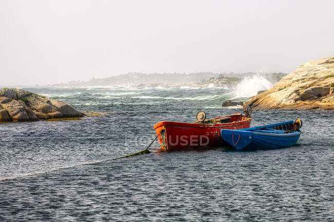 Два човни, що стоять на якорі в прибережній затоці з хвилями, що котяться по скелях на задньому плані. — стокове фото