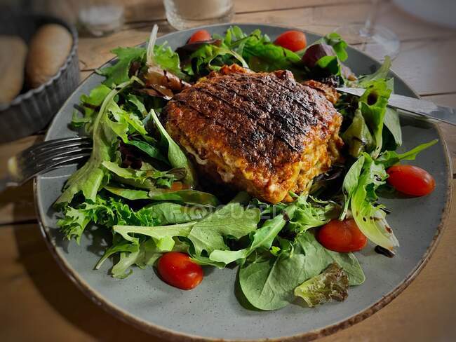 Lasagne with mixed leaf salad and tomatoes next to bread basket — Stock Photo
