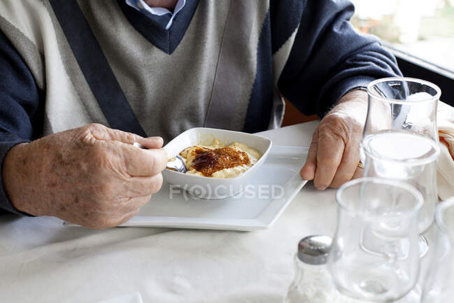 Hombre sentado en una mesa comiendo postre tradicional de arroz con leche turca (firin sutlac), Turquía - foto de stock