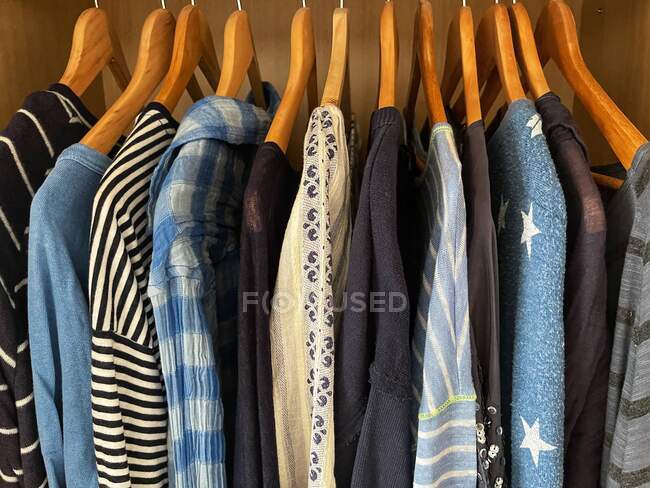 Разнообразные голубые топы, блузки, рубашки и футболки, висящие в шкафу — стоковое фото