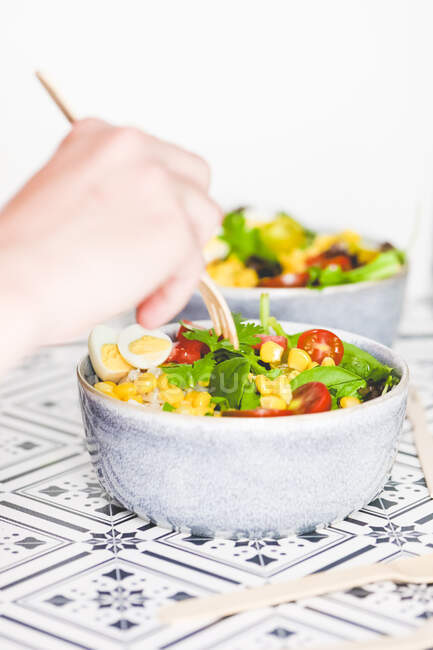 Человек, использующий вилку на тарелке салата с кукурузой, помидорами, рисом, кориандром и перепелиным яйцом — стоковое фото