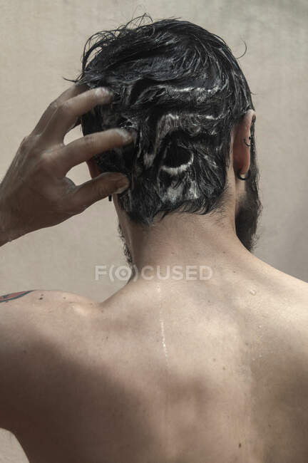 Vista trasera de un hombre de pie en la ducha lavándose el pelo - foto de stock