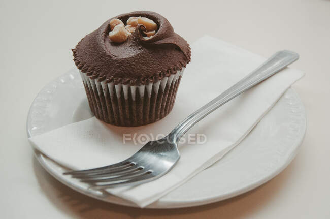 Cupcake au chocolat avec glaçage à la crème au beurre et noix sur assiette — Photo de stock