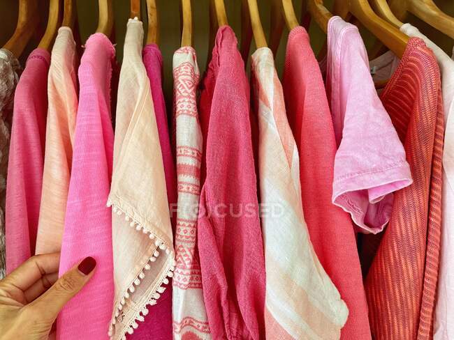 Weibliche Hand hält rosa Top mit anderen rosa Tops auf Kleiderbügeln — Stockfoto