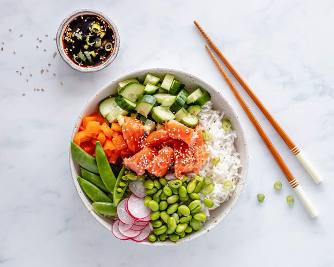 Salmon poke bowl with rice, edamame beans, cucumber, radish, mange tout, spring onion, bell peppers and soy dipping sauce — Stock Photo