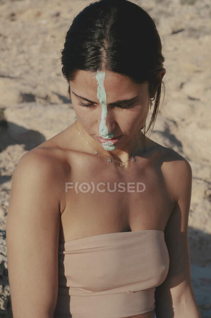 Donna con crema sul viso con un top a fascia seduta sulla spiaggia, Maiorca, Spagna — Foto stock
