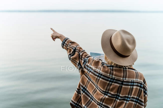 Vue arrière d'une femme debout au bord de la mer tenant une carte et pointant, Biélorussie — Photo de stock