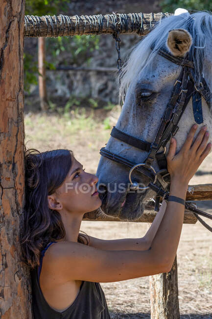 Femme debout face à face avec un cheval dans un champ tenant sa tête et regardant dans ses yeux, Italie — Photo de stock