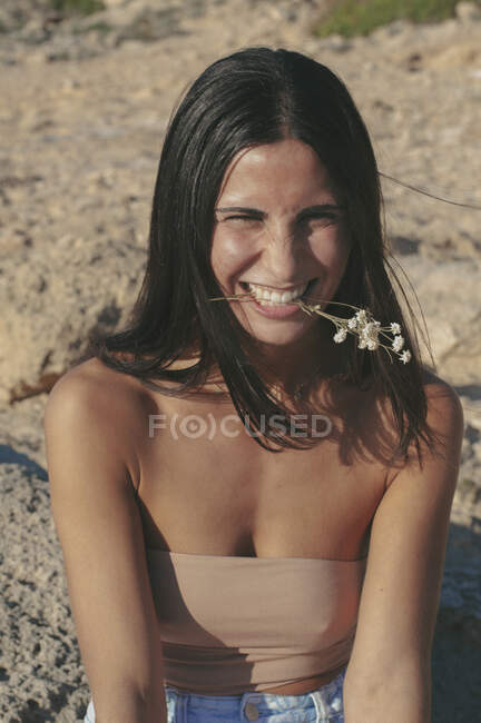 Улыбающаяся женщина, сидящая на пляже с цветочком во рту, Майя, Испания — стоковое фото