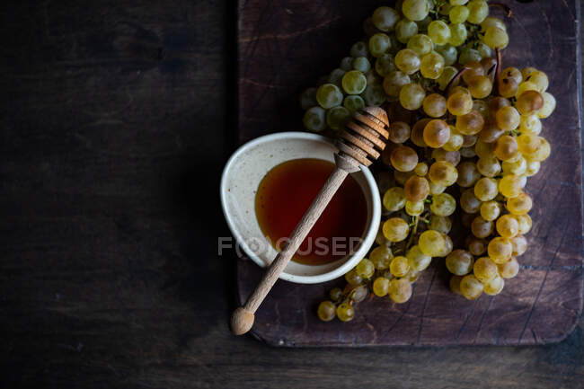 Bando de uvas ao lado da tigela de mel e mel dipper — Fotografia de Stock