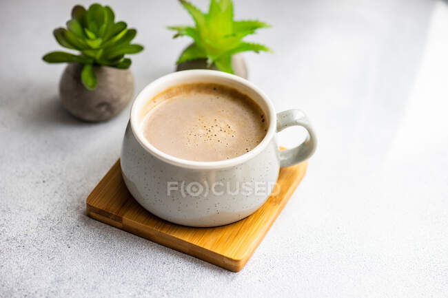 Cup of milky coffee next to two plants on a table — Stock Photo