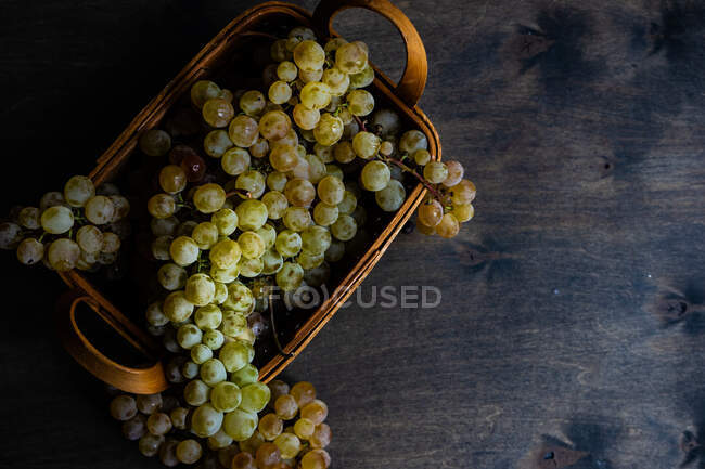 Grappolo d'uva su un tavolo accanto a un cesto pieno d'uva — Foto stock