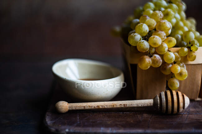 Pau de madeira e tigela de mel e uvas em caixa de madeira — Fotografia de Stock