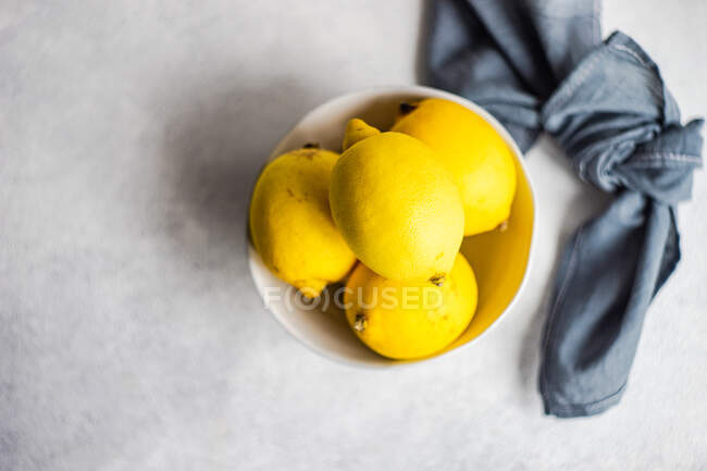 Bowl of fresh lemons with cloth napkin on concrete surface — Stock Photo