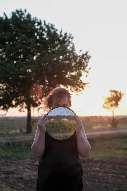 Porträt einer Frau, die auf einem Feld steht und einen Spiegel vor ihrem Gesicht hält, Frankreich — Stockfoto