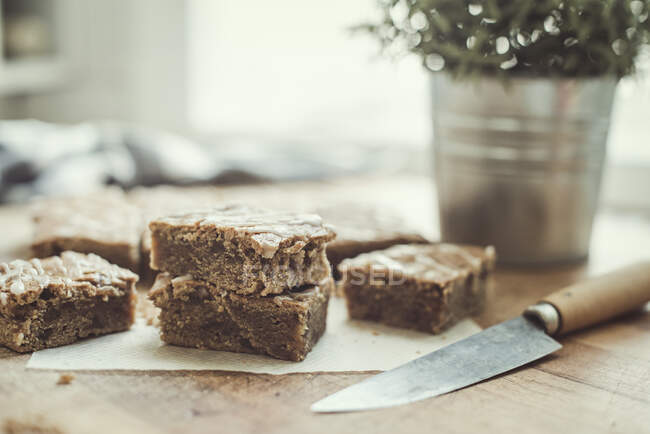 Homemade caramel blondie bars on wooden table with knife, and potted plant — Stock Photo