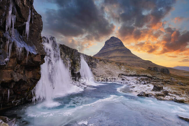 Riesiger Wasserfall in verschneiter Landschaft mit Felsen und Sonnenuntergang — Stockfoto