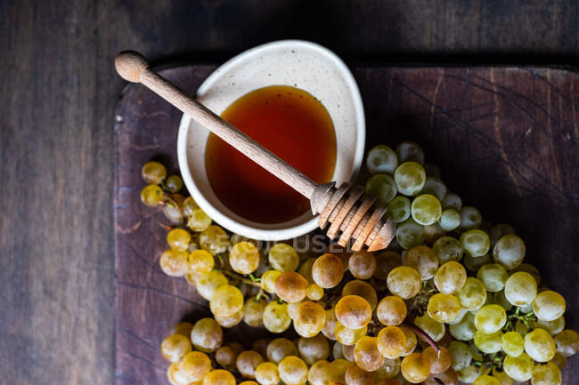 Зверху видніється мед у чаші з палицею і виноградом на дерев 