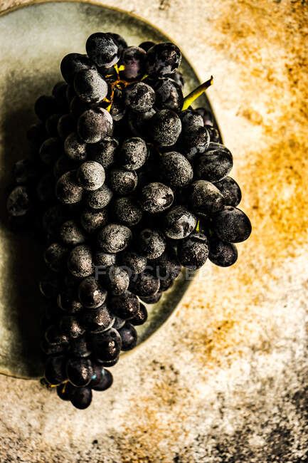 Bunch of black grapes on late on rustic surface — Stock Photo