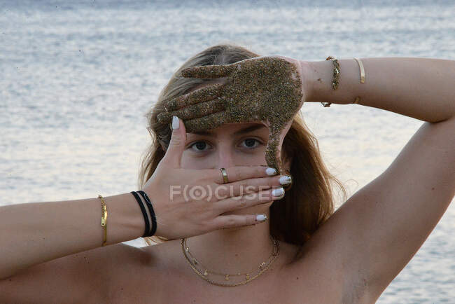Портрет девочки-подростка, стоящей на пляже и смотрящей сквозь свои песчаные руки, Греция — стоковое фото