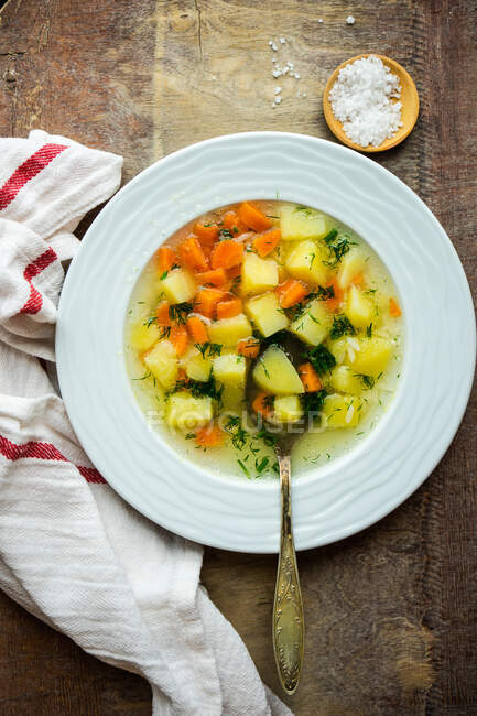 Bol de soupe aux carottes et pommes de terre avec de l'aneth sur la table avec du sel de mer frais et un torchon — Photo de stock