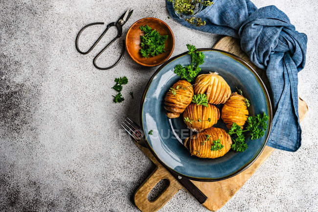 Ciotola di patate hasselback con prezzemolo fresco su superficie di pietra — Foto stock