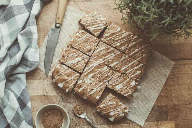 Homemade caramel blondie bars on wooden table with knife, tea towel and pot plant — Stock Photo