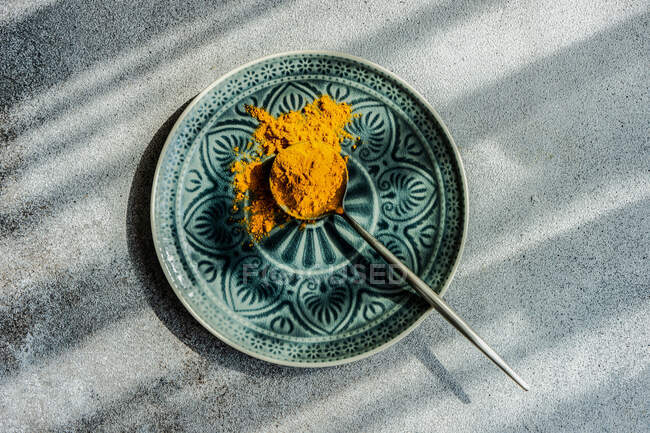 Cucchiaio di curcuma in polvere sul piatto alla luce del sole — Foto stock