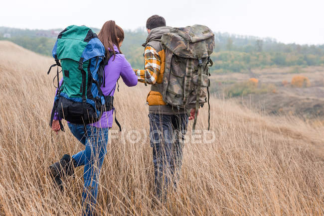 Coppia giovane con zaini passeggiando in campagna — Foto stock