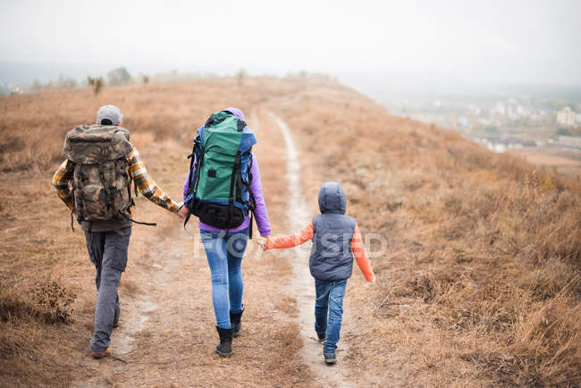 Famiglia con zaini che camminano sul sentiero rurale — Foto stock