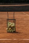 Basket of tennis balls standing on court — Stock Photo