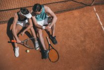 Высокий угол зрения молодой пары опираясь на сетку и расслабляясь на теннисном корте — стоковое фото