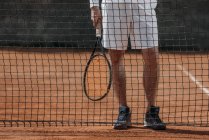 Cropped shot of tennis player with racket standing behind net — Stock Photo